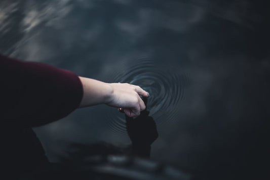 Hand touching water creating ripples - karma as cause and effect