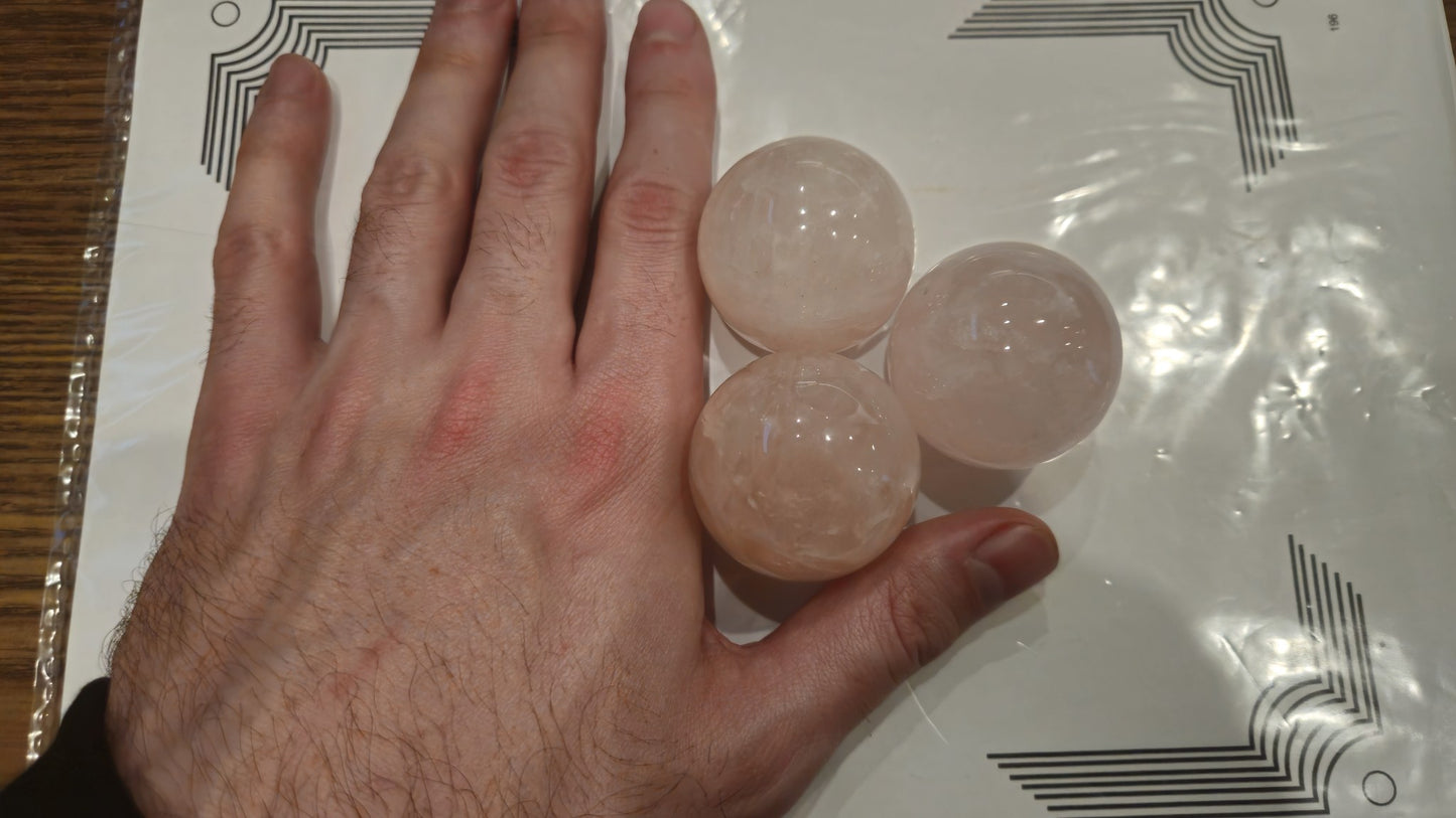 Three 40mm rose quartz spheres in hand showing scale reference