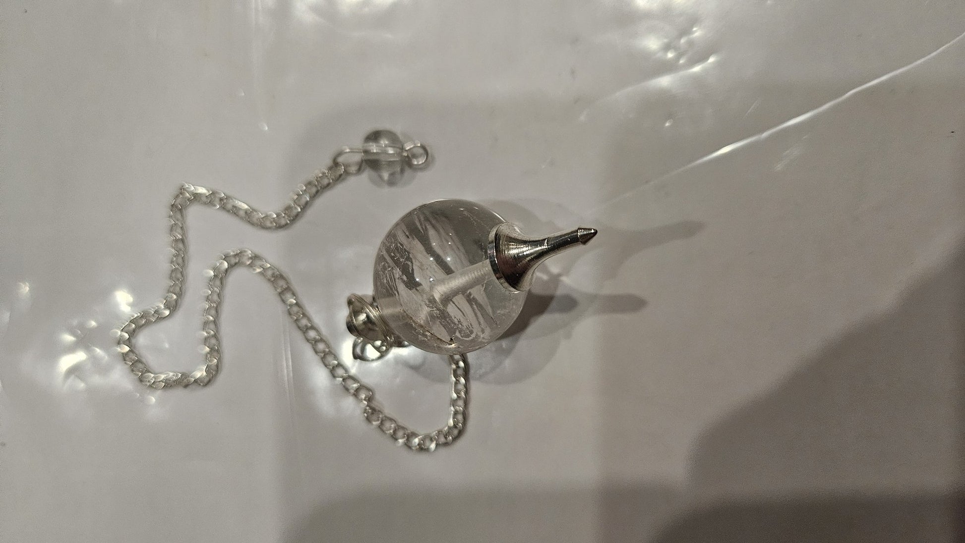 Clear quartz ball pendulum detail view with silver cap and chain
